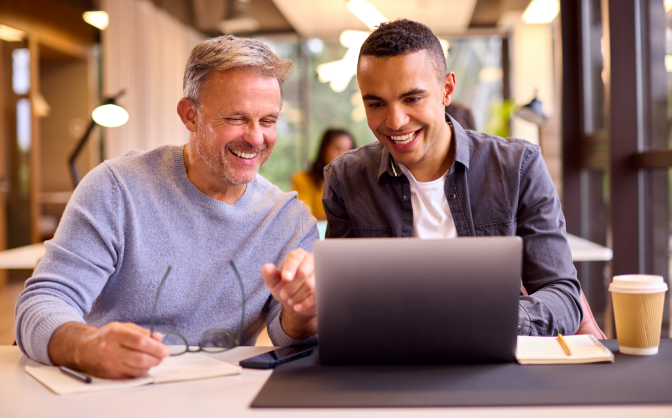 Foto de un joven y un hombre adulto en un café, ubicados en una mesa con un computador portátil donde leen los distintos fondos de inversión para decidir los mejores fondos de inversión colectiva para ellos.